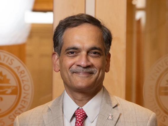 Suresh Garimella standing in front of a glass doorway with the seal of the University of Arizona over each shoulder and a wood-paneled hallway behind him. 