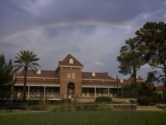 A large building sits under a cloudy sky with a rainbow overhead.