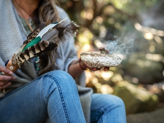 two hands holding a feather and a bowl during a smudging ceremony