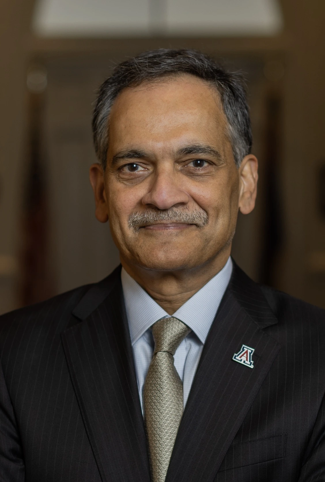 Portrait of President Garimella wearing a blue blazer, tie, and a block A logo lapel pin.