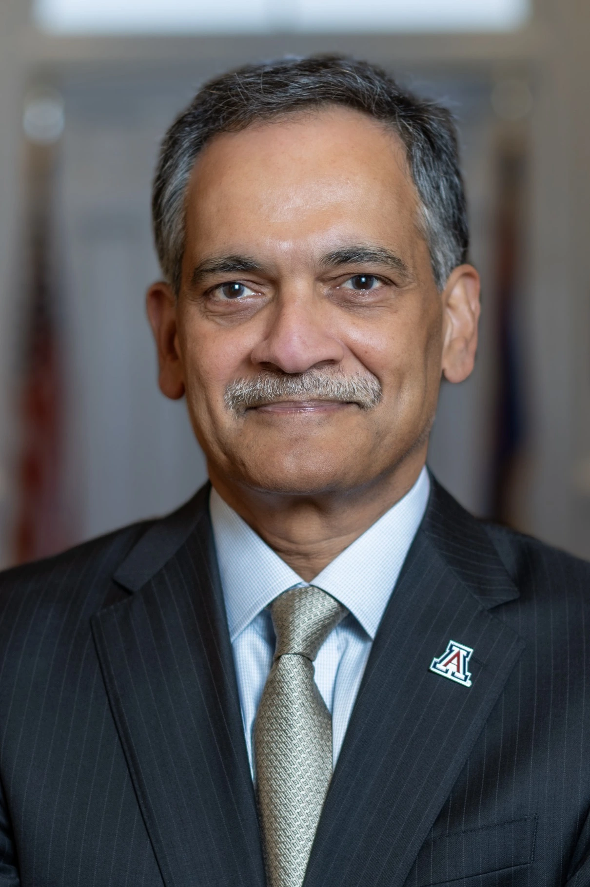 Portrait of President Garimella wearing a blue blazer, tie, and a block A logo lapel pin.